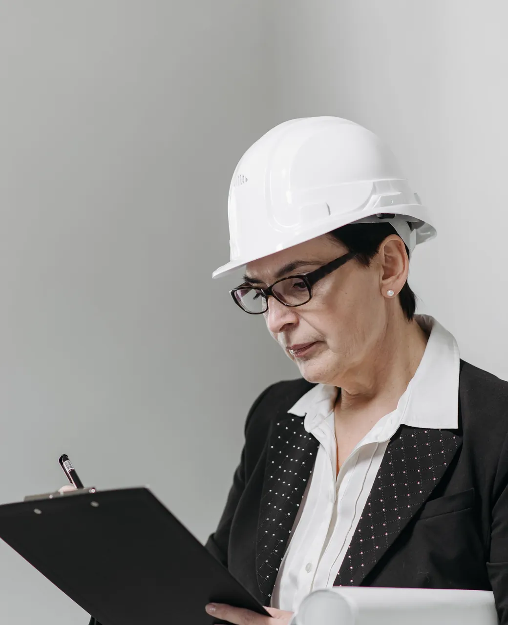 Architecte casquée relevant des notes sur un presse-papiers avec des plans sous le bras