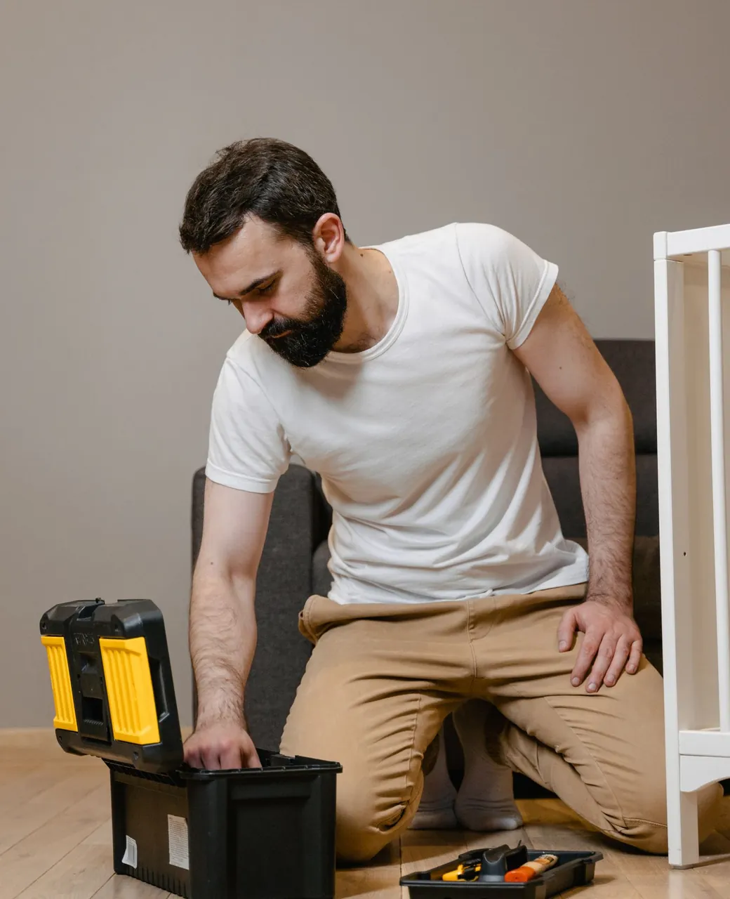 Artisan multiservices agenouillé près de sa caisse à outils dans un logement