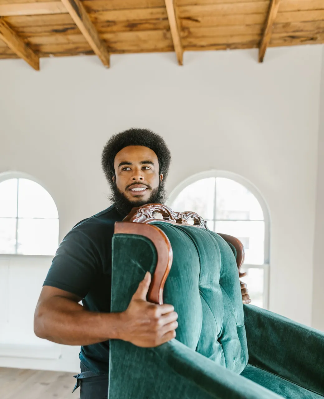 Déménageur souriant portant un fauteuil vert dans un logement vide