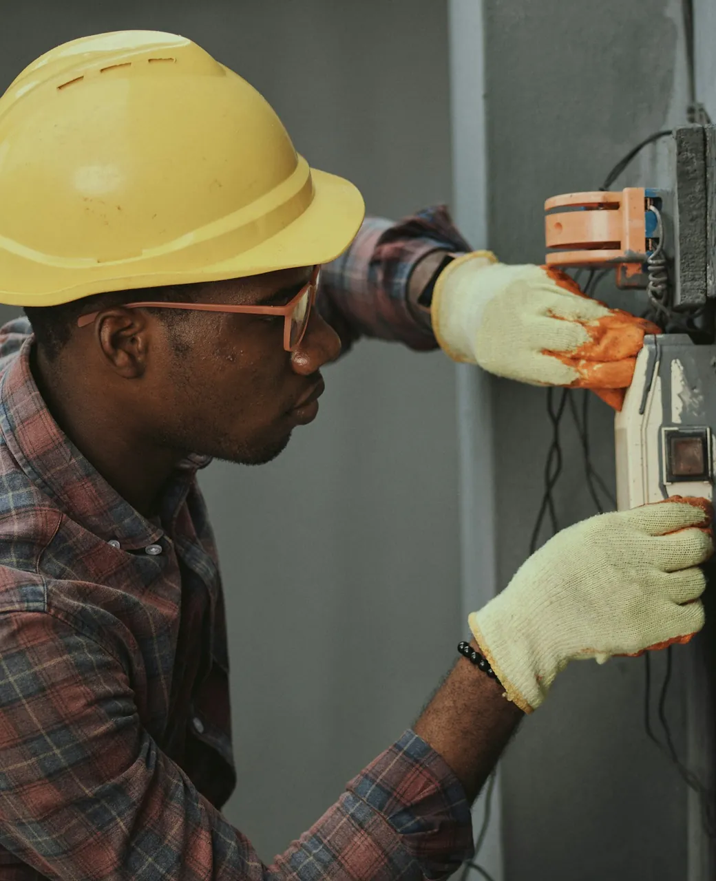 Électricien casqué et ganté intervenant sur un coffret électrique mural