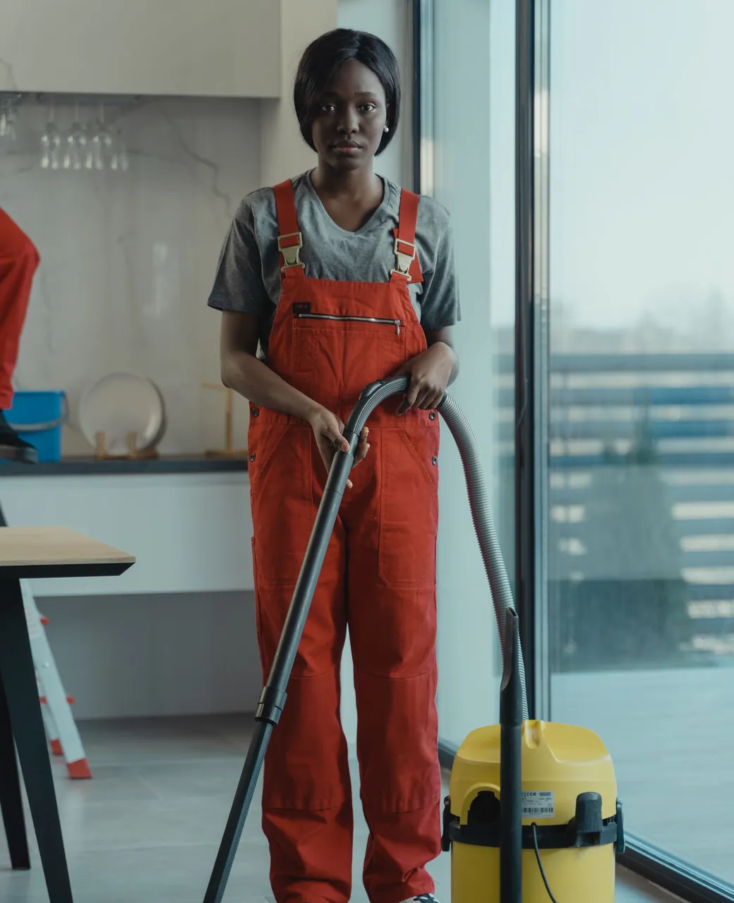 Agente de nettoyage en salopette orange avec son aspirateur dans des bureaux lumineux