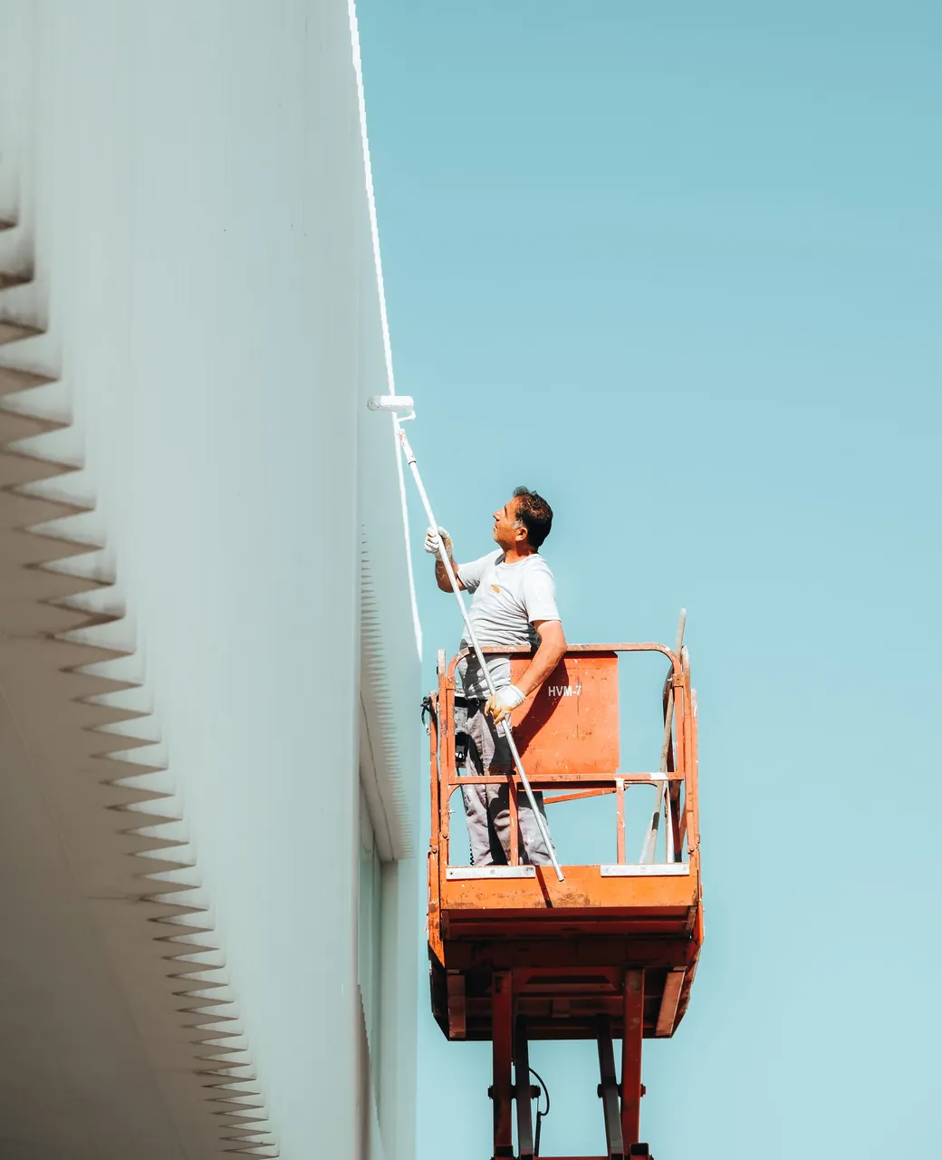 Façadier sur une nacelle élévatrice peignant une façade blanche avec un rouleau télescopique