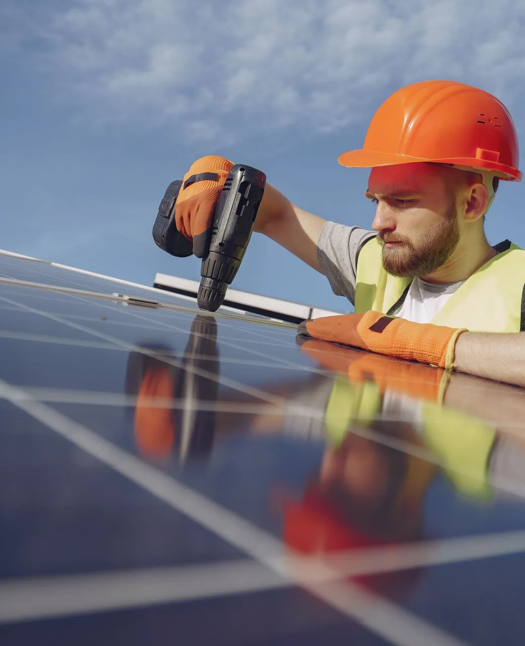 Installateur photovoltaïque casqué vissant un panneau solaire sur une toiture