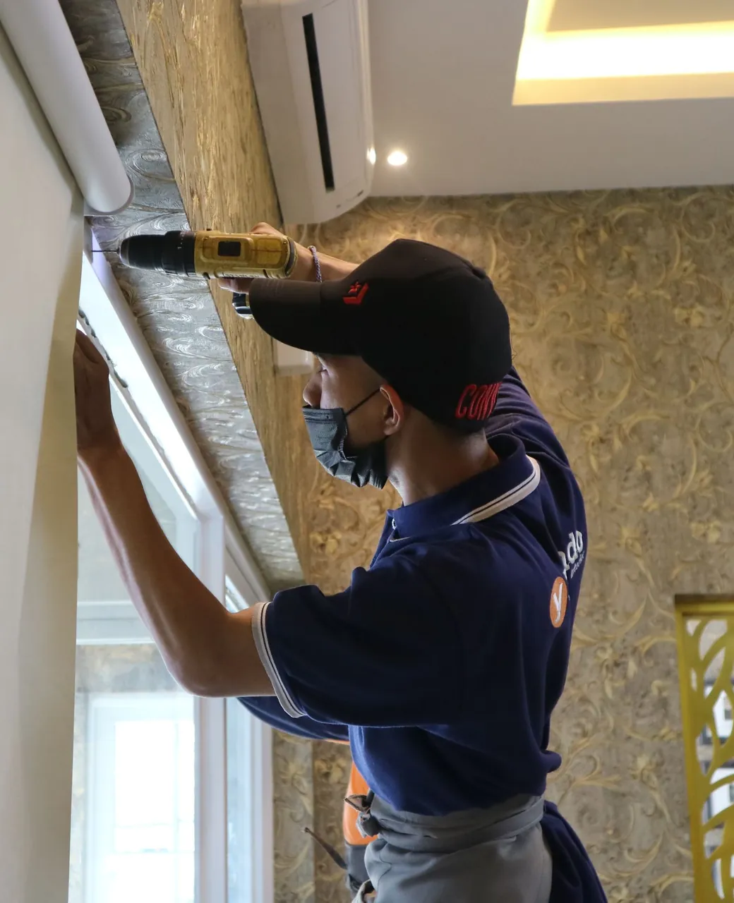 Installateur fixant à la visseuse le rail d’un store au-dessus d’une fenêtre
