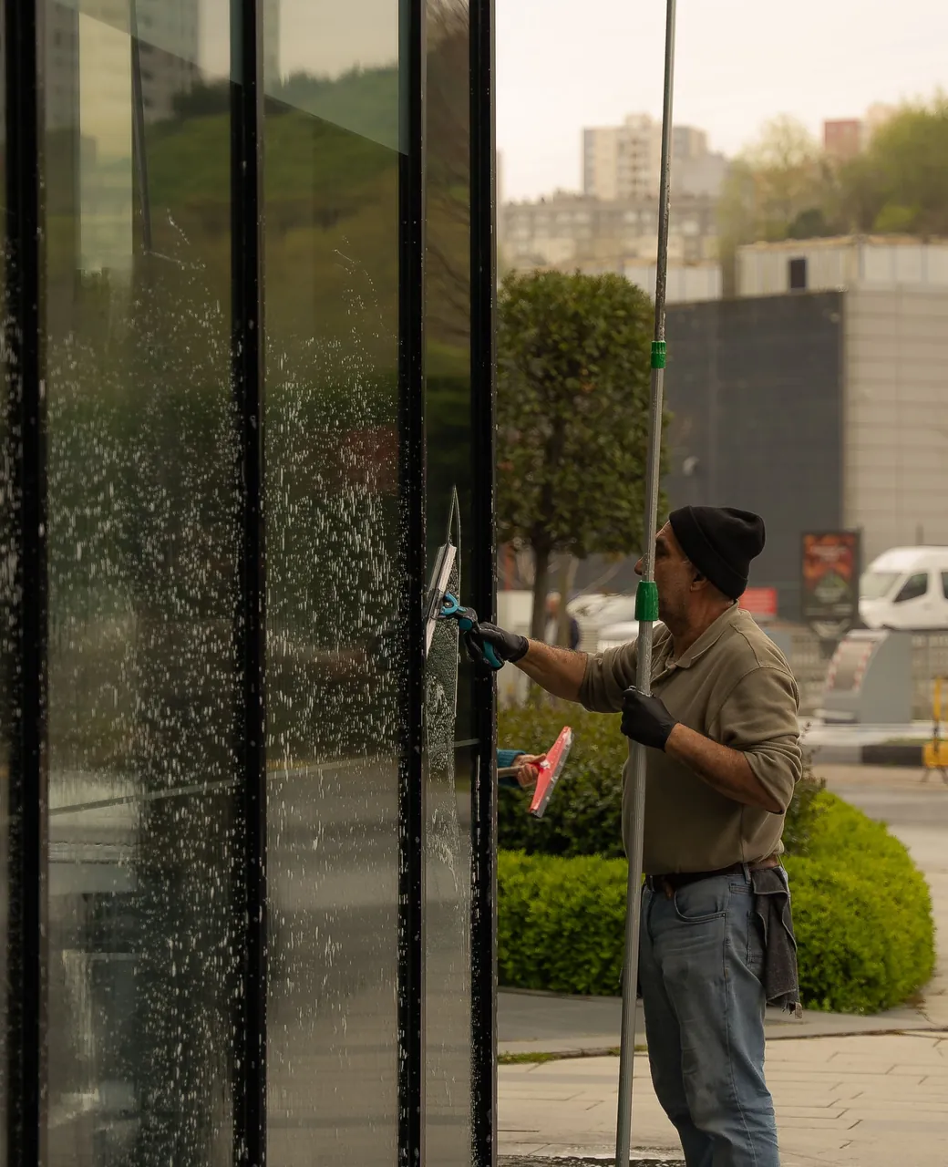 Laveur de vitres nettoyant une grande façade vitrée avec une perche et une raclette