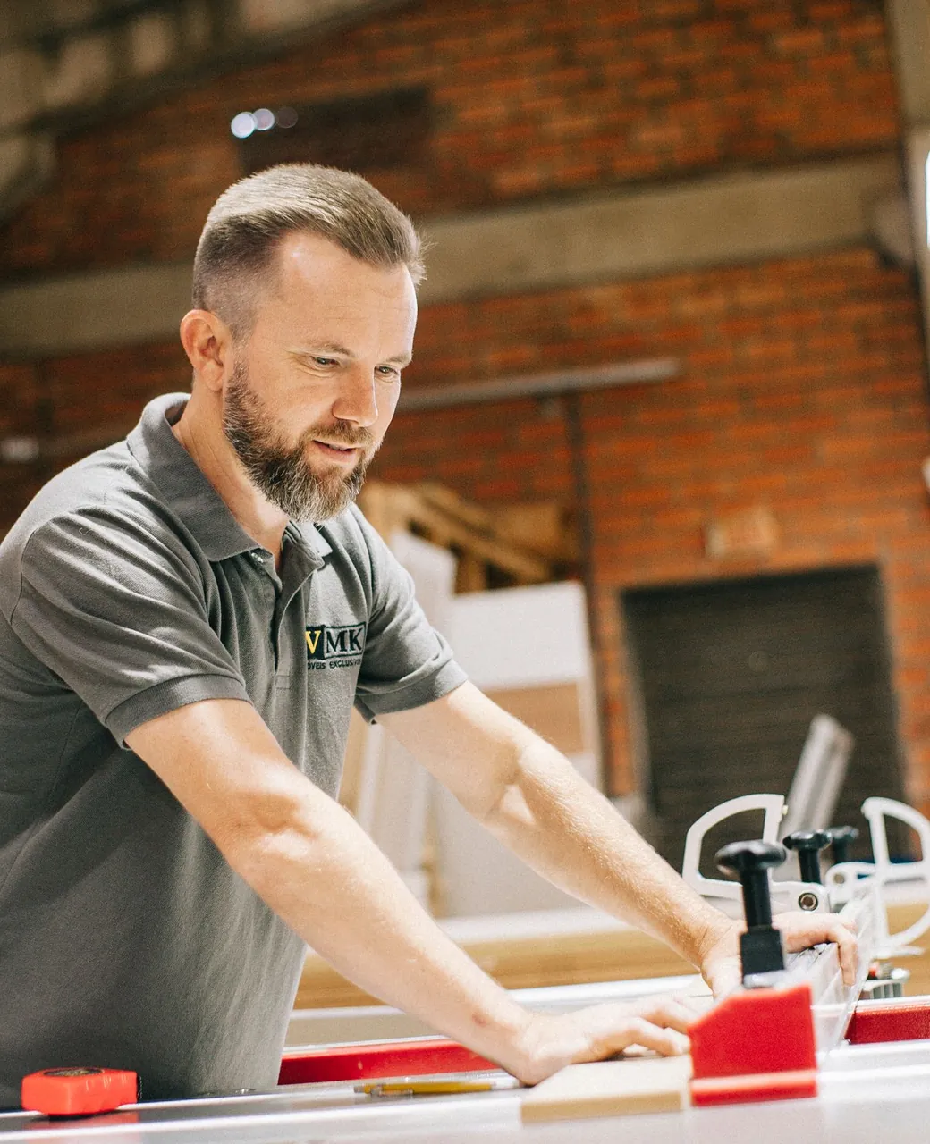 Menuisier en polo gris travaillant une planche sur sa scie de table dans son atelier