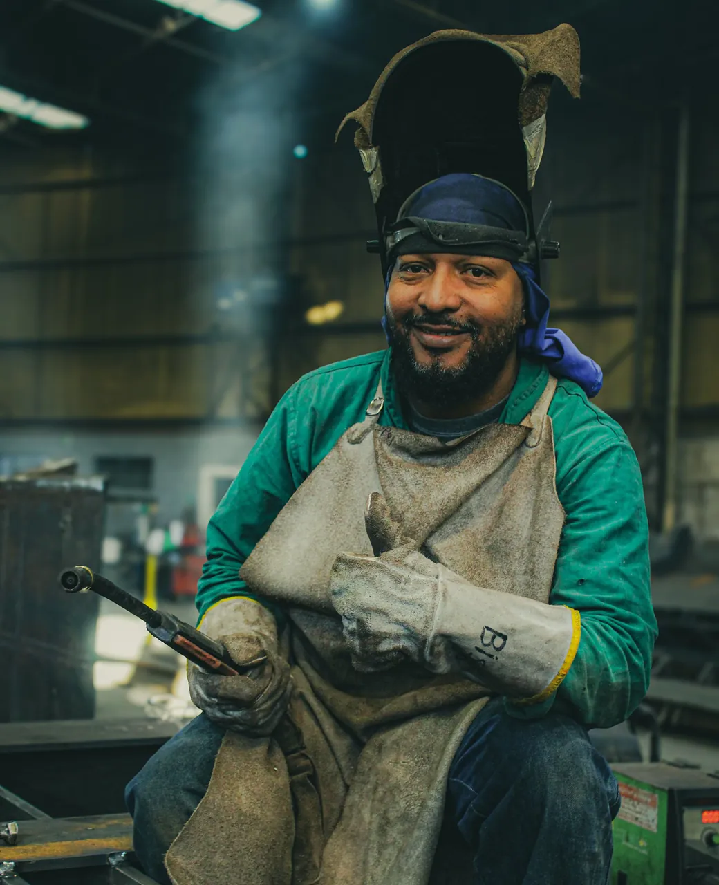 Métallier souriant en tablier de soudeur, casque relevé, dans son atelier