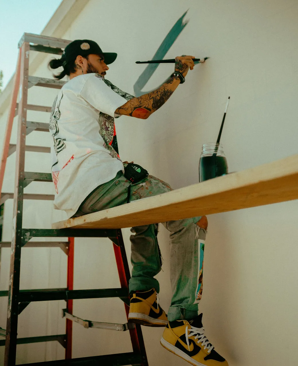 Peintre en bâtiment sur une échelle, pinceau à la main, peignant un mur blanc