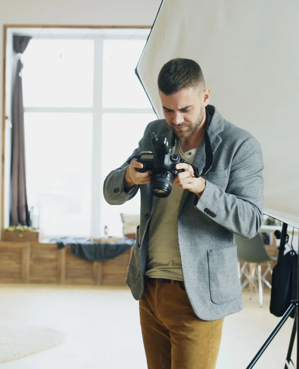 Photographe en veste grise cadrant avec un reflex dans un studio lumineux
