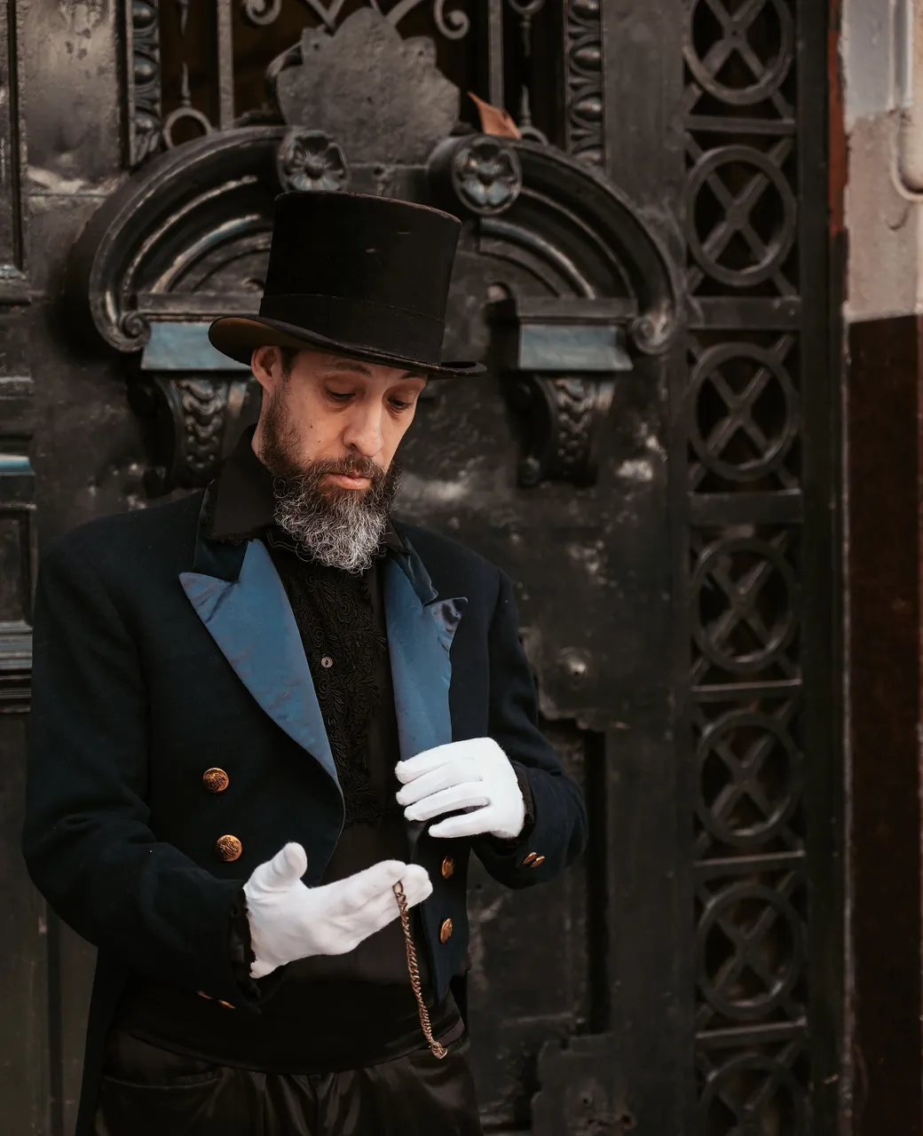 Ramoneur en tenue traditionnelle noire, haut-de-forme et gants blancs, devant une porte ouvragée