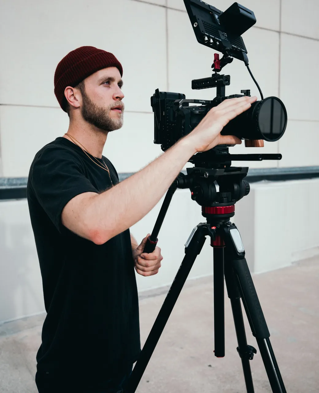 Vidéaste en bonnet réglant une caméra de cinéma montée sur trépied