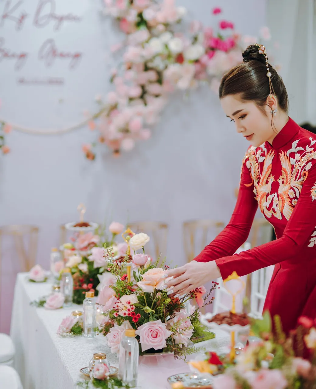 Wedding planner en robe rouge disposant des fleurs sur une table de réception